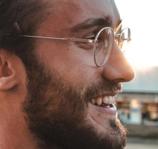 Mann mit Brille lächelt, während er vor einem Geschäft steht. 